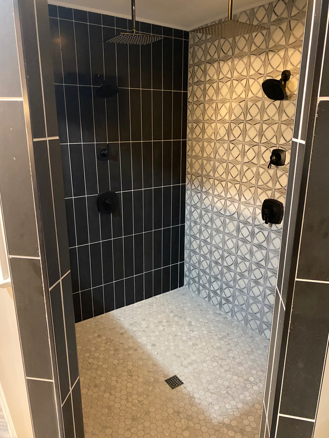 A walk in shower with black and white tiles and a shower head.