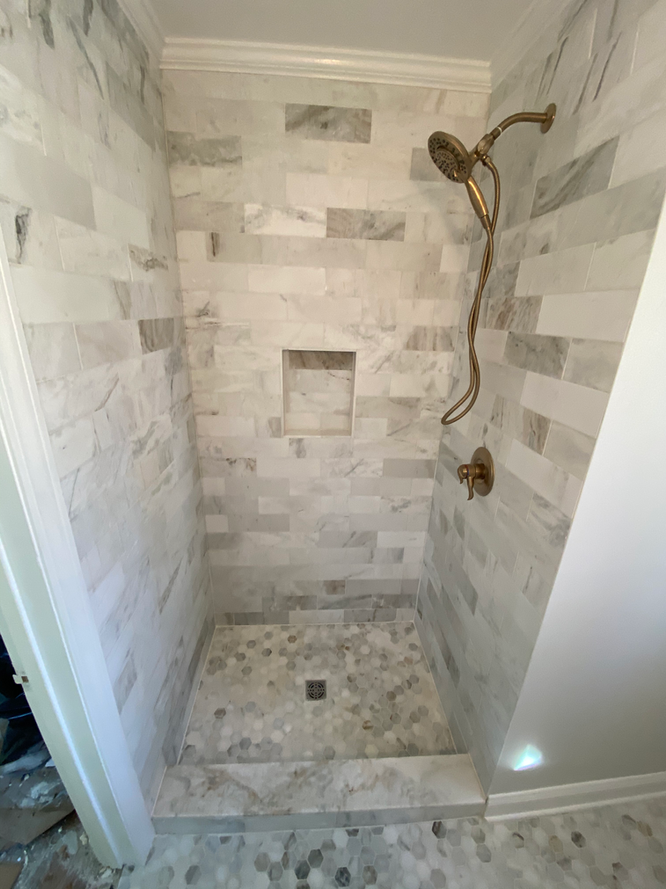 A shower stall with marble tiles and a gold shower head.