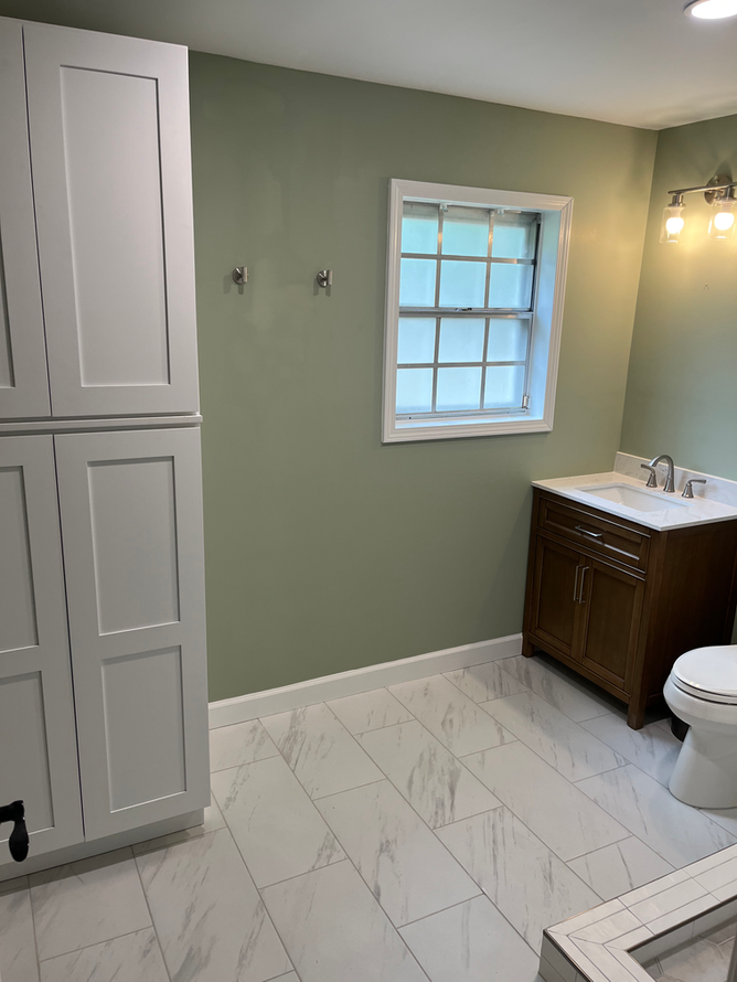 A bathroom with a toilet , sink , cabinets and a window.