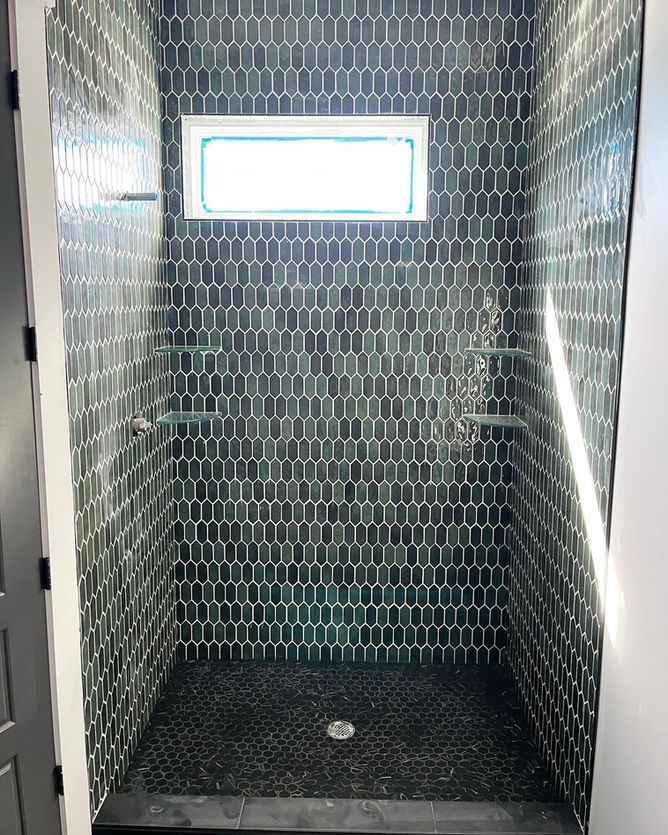 A shower stall with black tiles and a window.