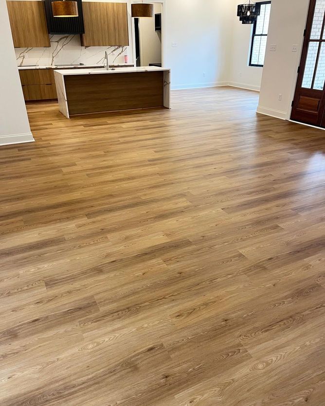 A living room with a wooden floor and a kitchen in the background.