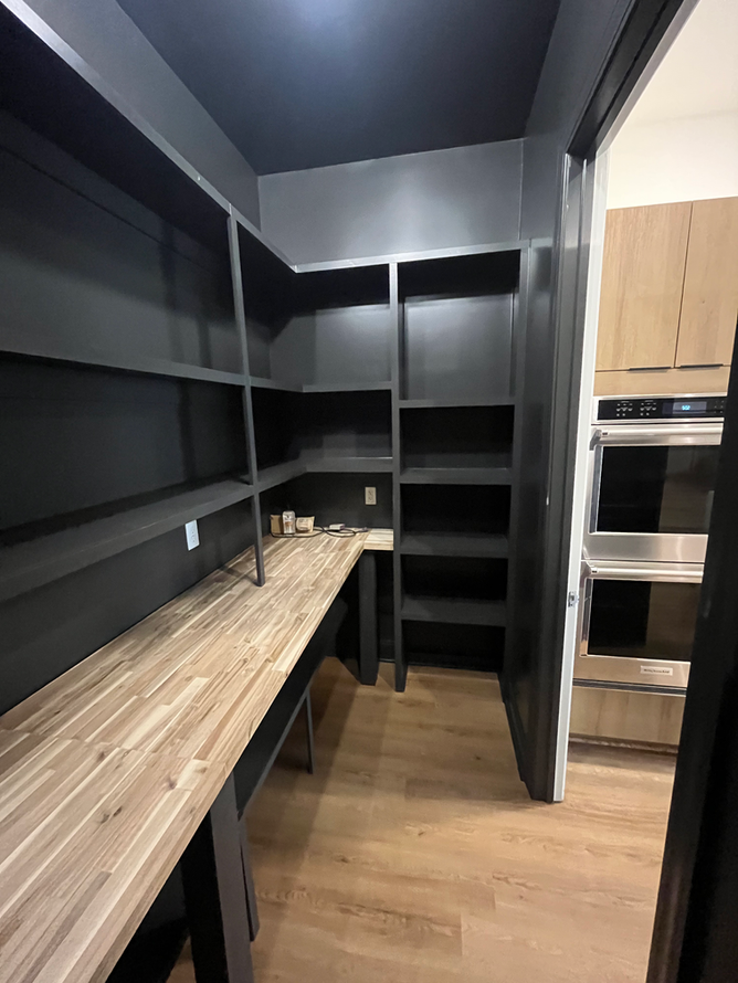 A pantry with a wooden counter top and black shelves