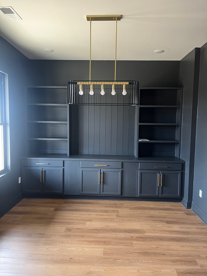 An empty room with black cabinets and shelves and a chandelier hanging from the ceiling.