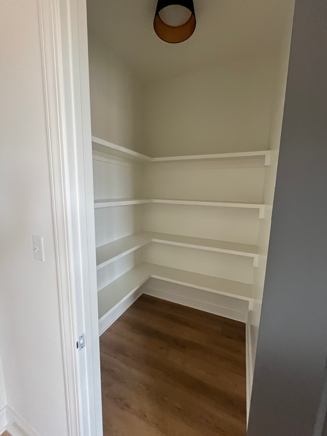 A closet with white shelves and wooden floors in a house.