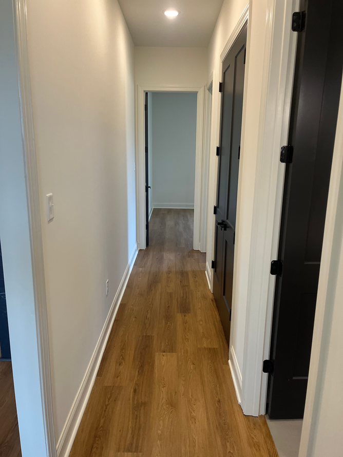 A long hallway with hardwood floors and black doors in a house.