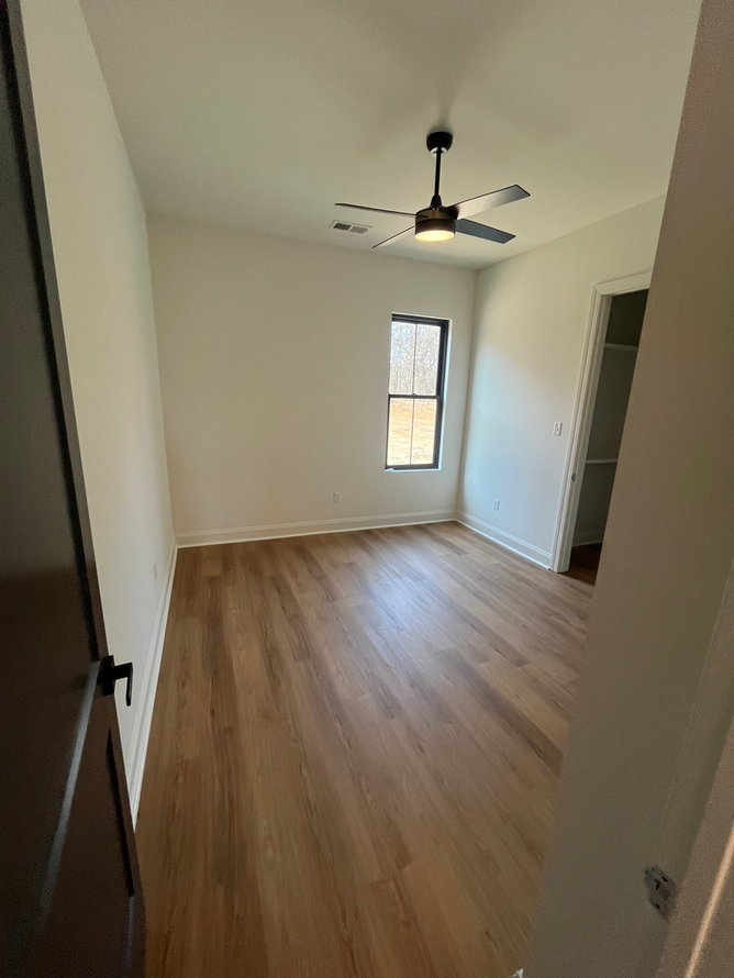 An empty bedroom with hardwood floors and a ceiling fan.