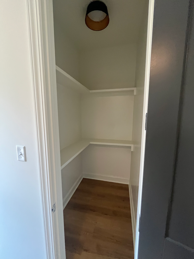 A small closet with wooden floors and shelves in a house.