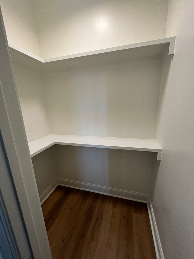 A small closet with hardwood floors and white shelves.