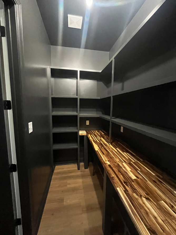 A walk in pantry with wooden shelves and a wooden counter top.