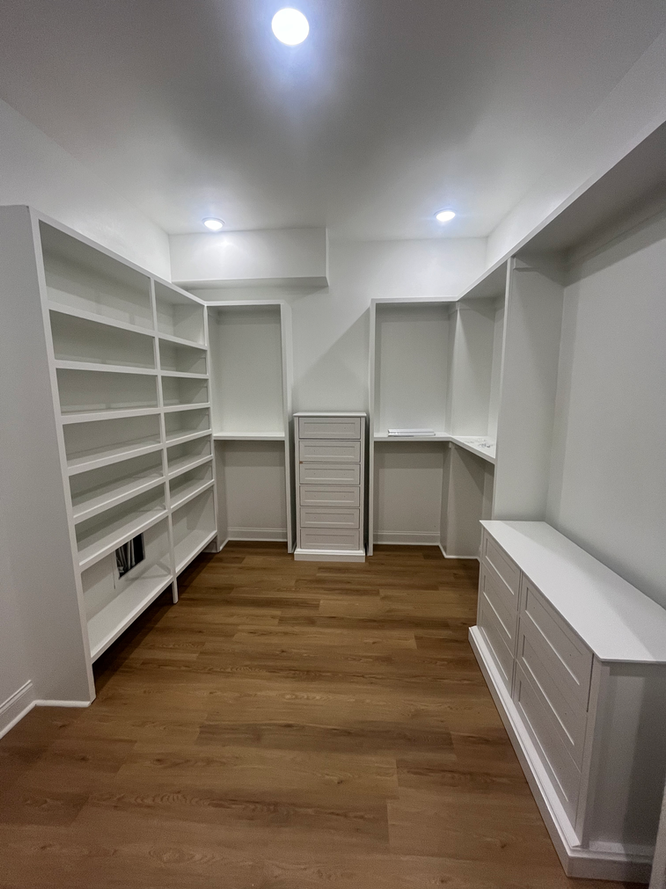 A walk in closet with white shelves and wooden floors.
