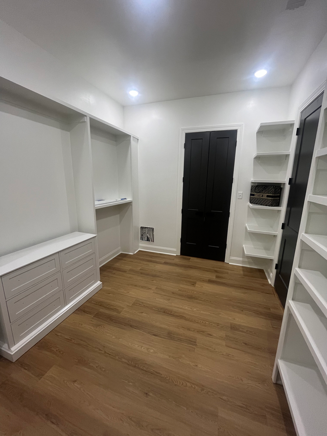 A walk in closet with hardwood floors and white shelves.