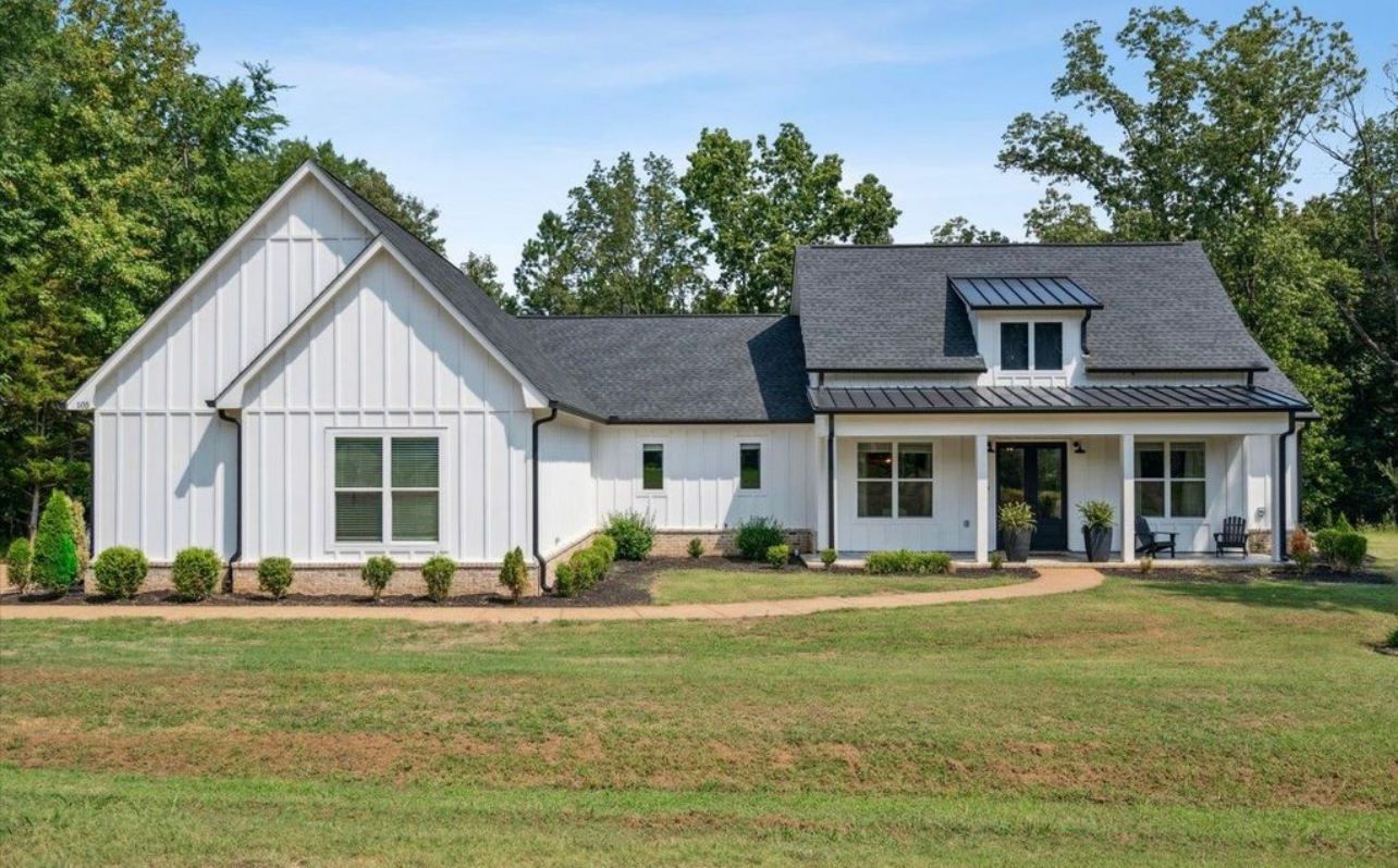 A white house with a black roof is sitting on top of a lush green field.