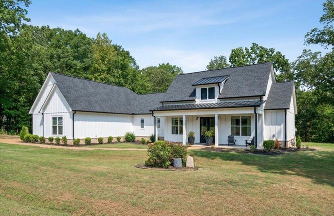 A white house with a black roof is sitting on top of a lush green field.