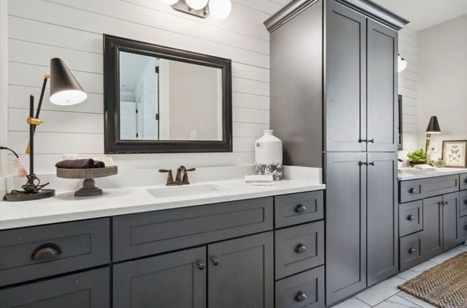 A bathroom with two sinks , a mirror , and gray cabinets.