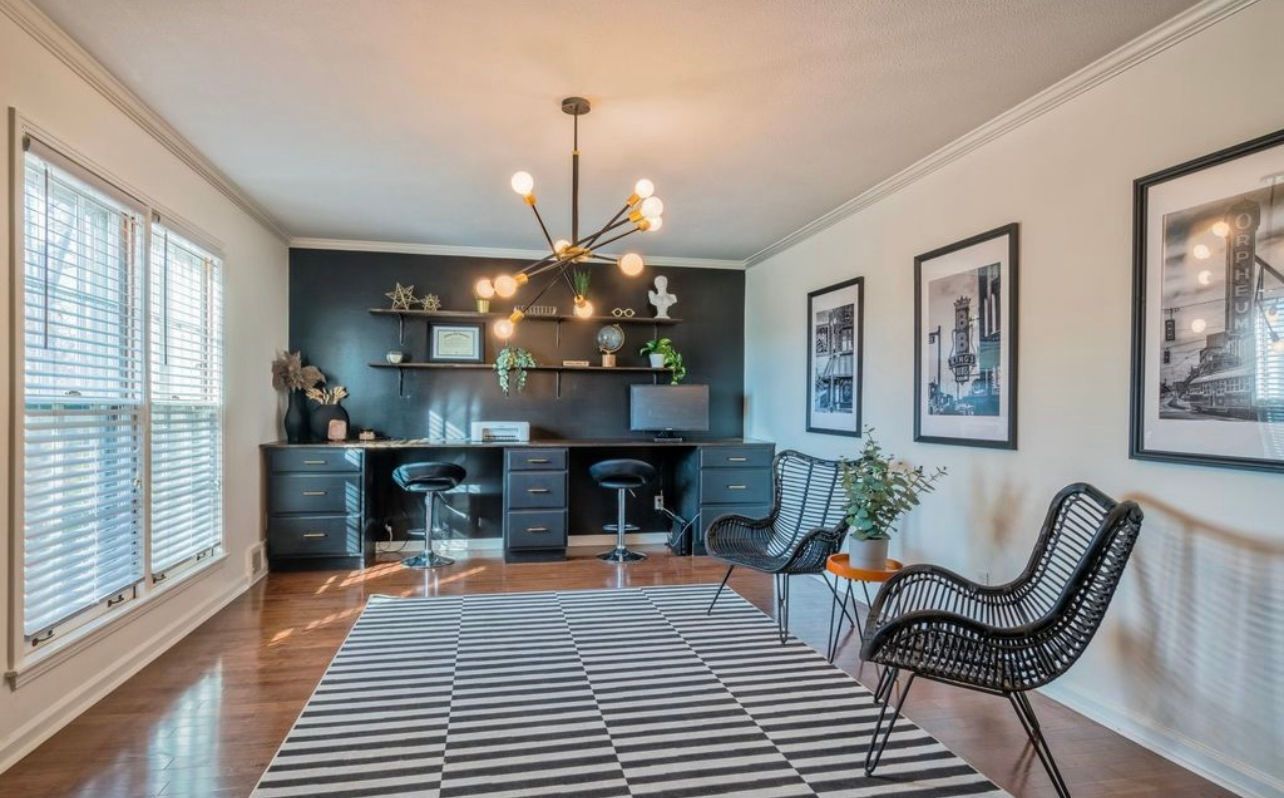 A living room with a rug , chairs , desks and a chandelier.