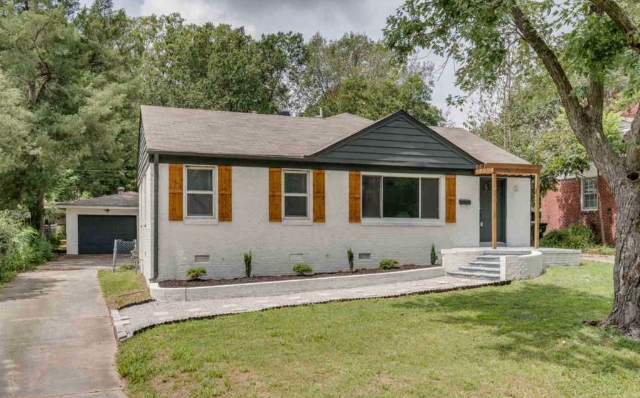 A white house with a black roof and orange shutters is for sale.