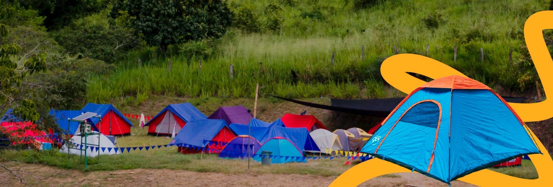 Tiendas de campaña instaladas en una zona cubierta de hierba frente a una ladera verde.