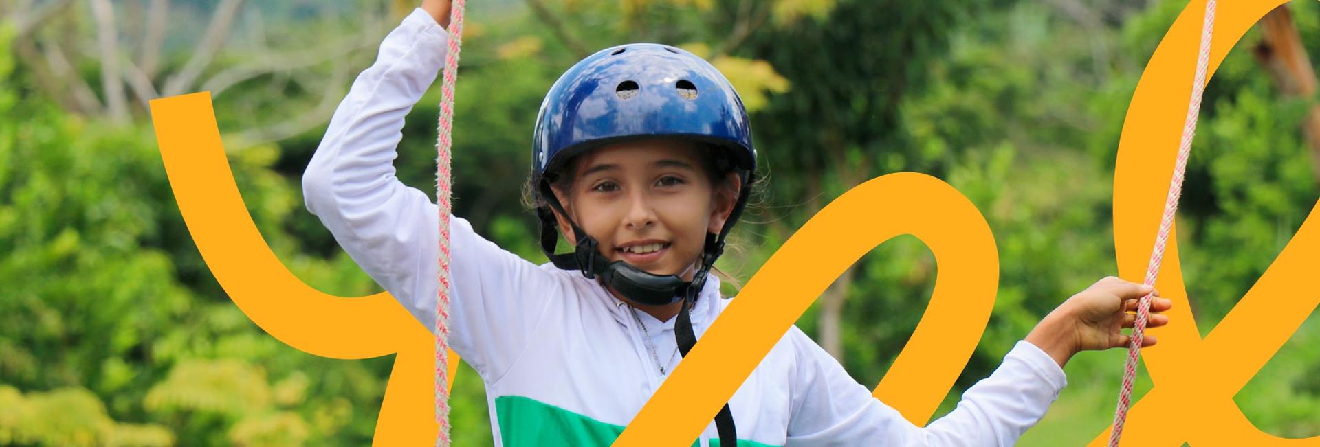 Niño con casco, sosteniendo cuerdas al aire libre, sonriendo. Camisa verde y blanca. Superposición gráfica amarilla.