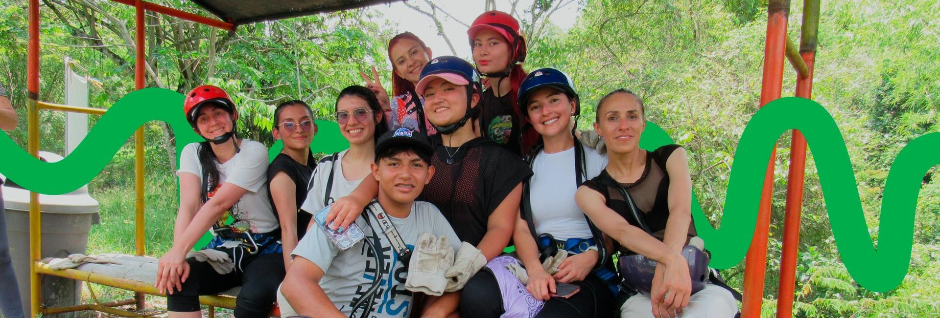Un grupo de personas con cascos y arneses sonríe para una foto al aire libre. Árboles verdes al fondo.