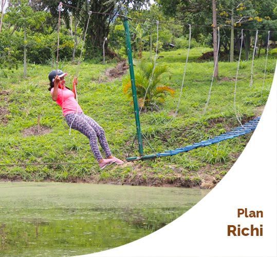 Mujer balanceándose en una tirolina sobre el agua, rodeada de vegetación.