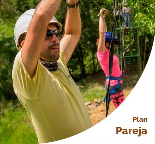 Hombre y mujer practicando tirolesa, con casco y arneses. Texto