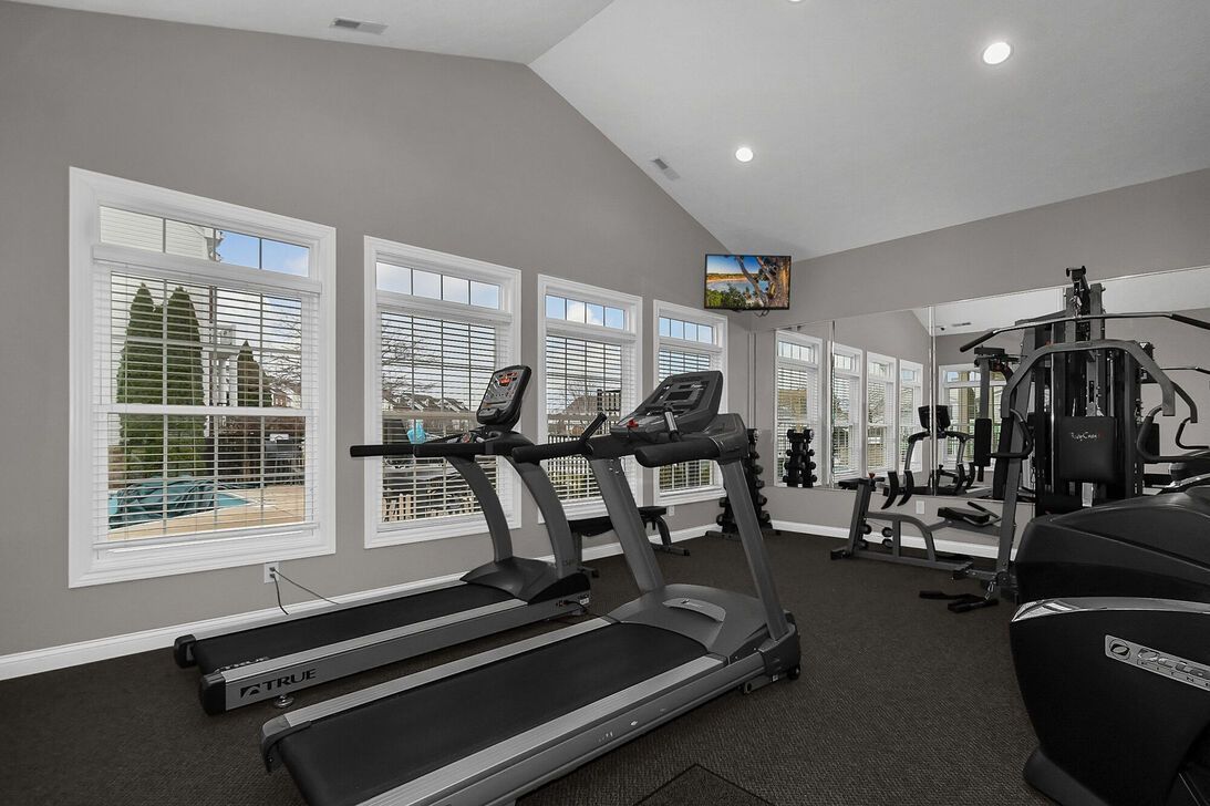 Bright home gym with treadmills, weights, and large windows letting in daylight