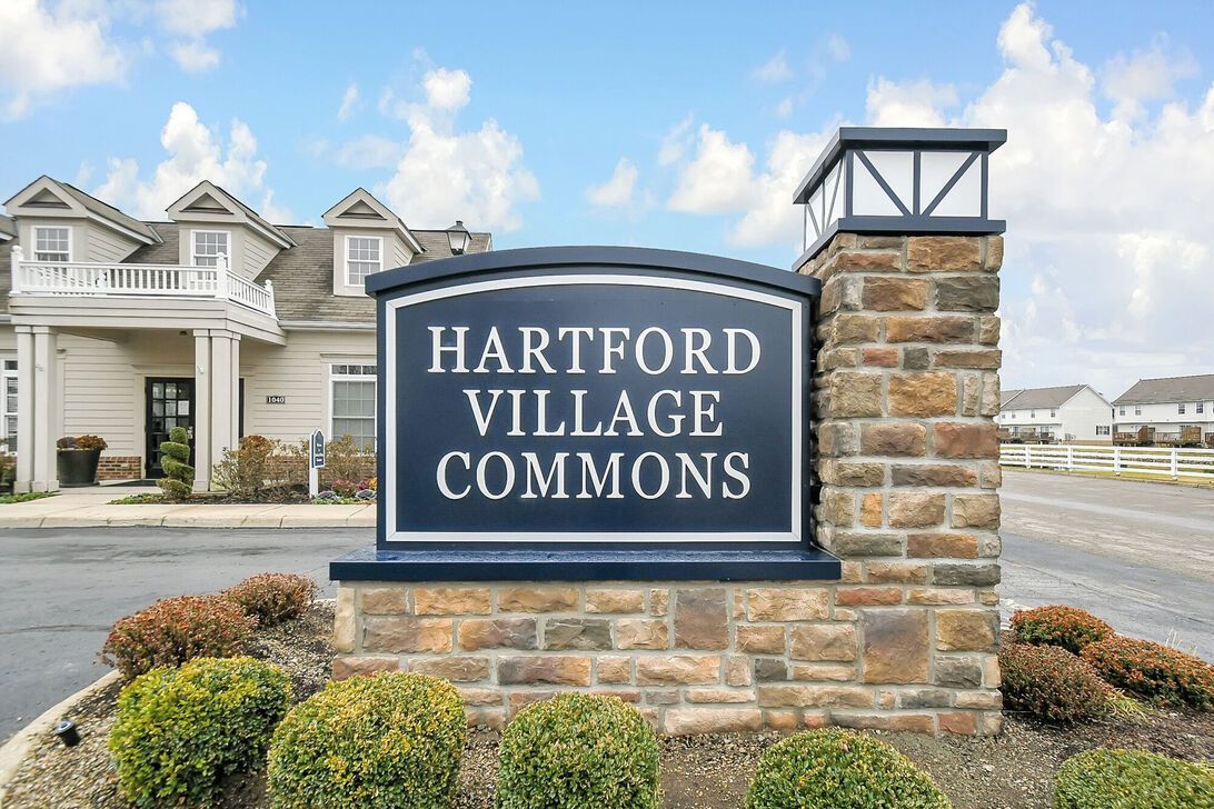 Hartford Village Commons entrance sign on a stone monument beside townhomes and a roadway