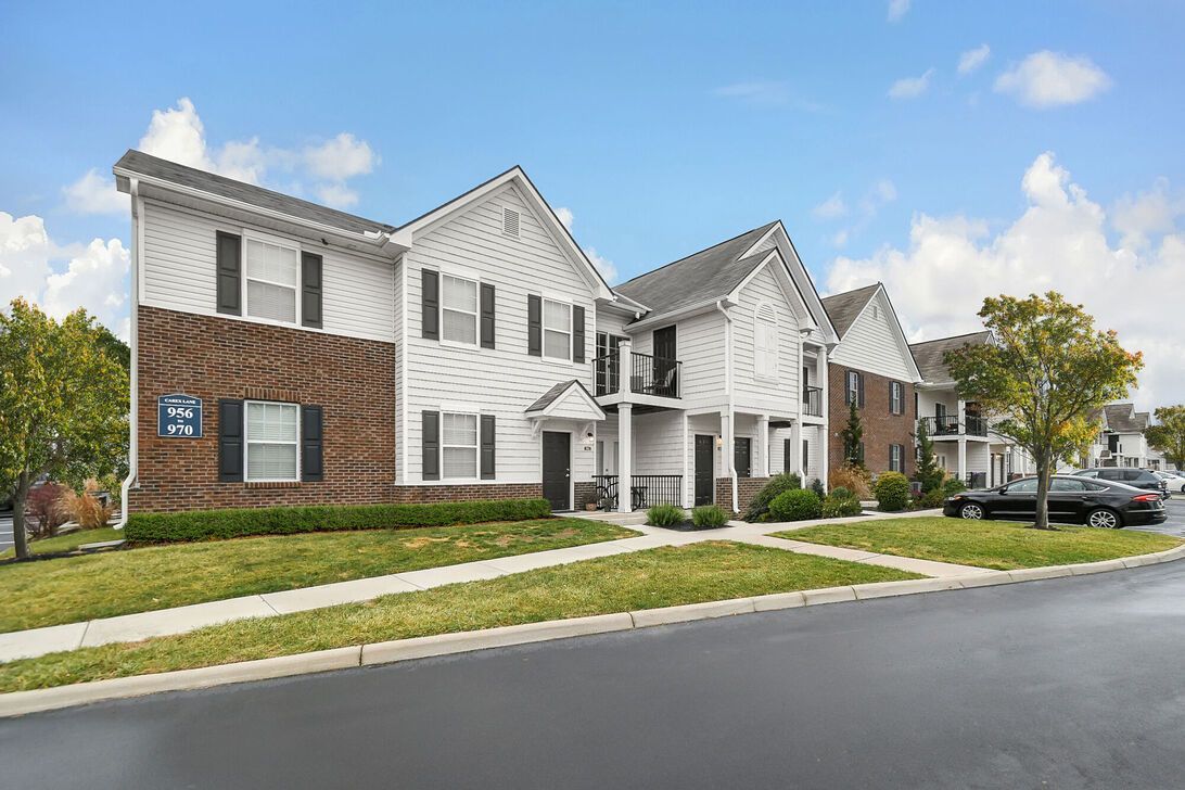 Row of modern townhouses with white siding and brick accents along a quiet street under a blue sky
