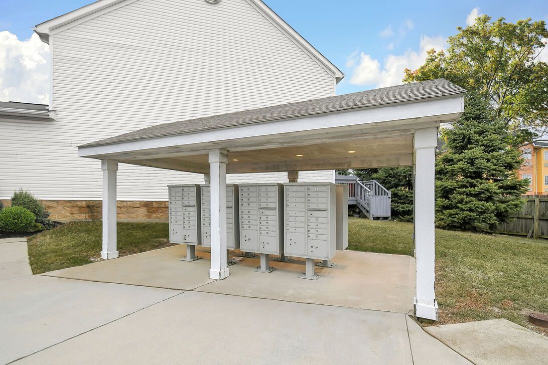 Covered apartment mailboxes beside a concrete walkway and grassy lawn