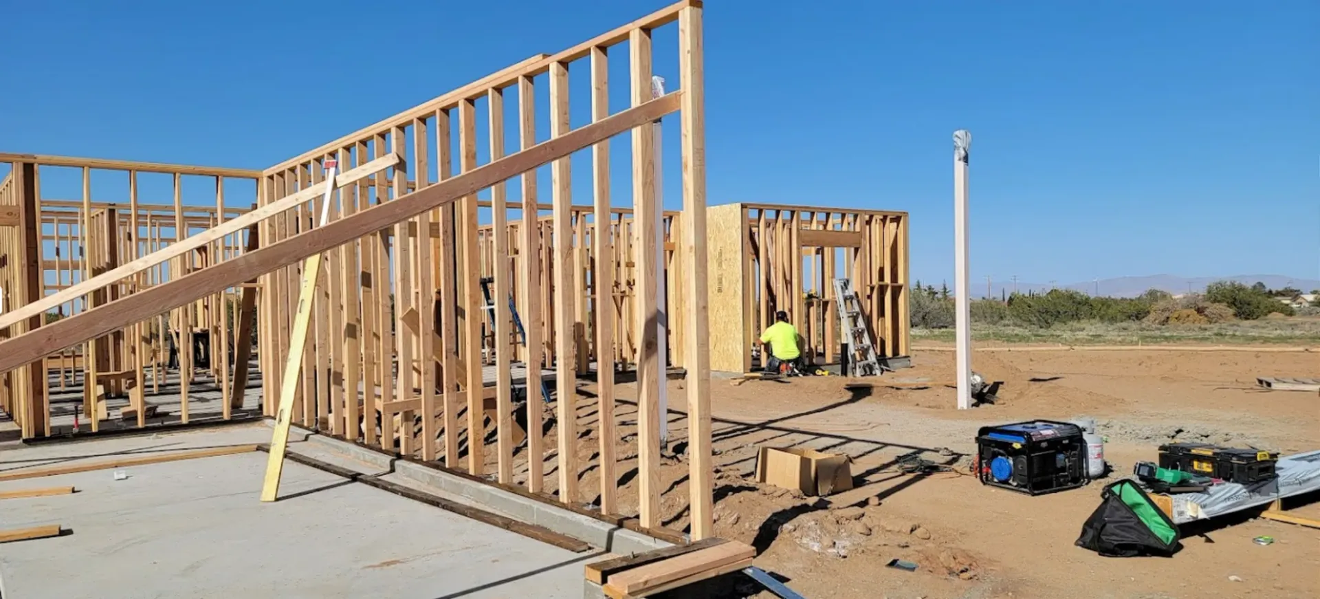 A house is being built on a dirt field with a blue sky in the background.