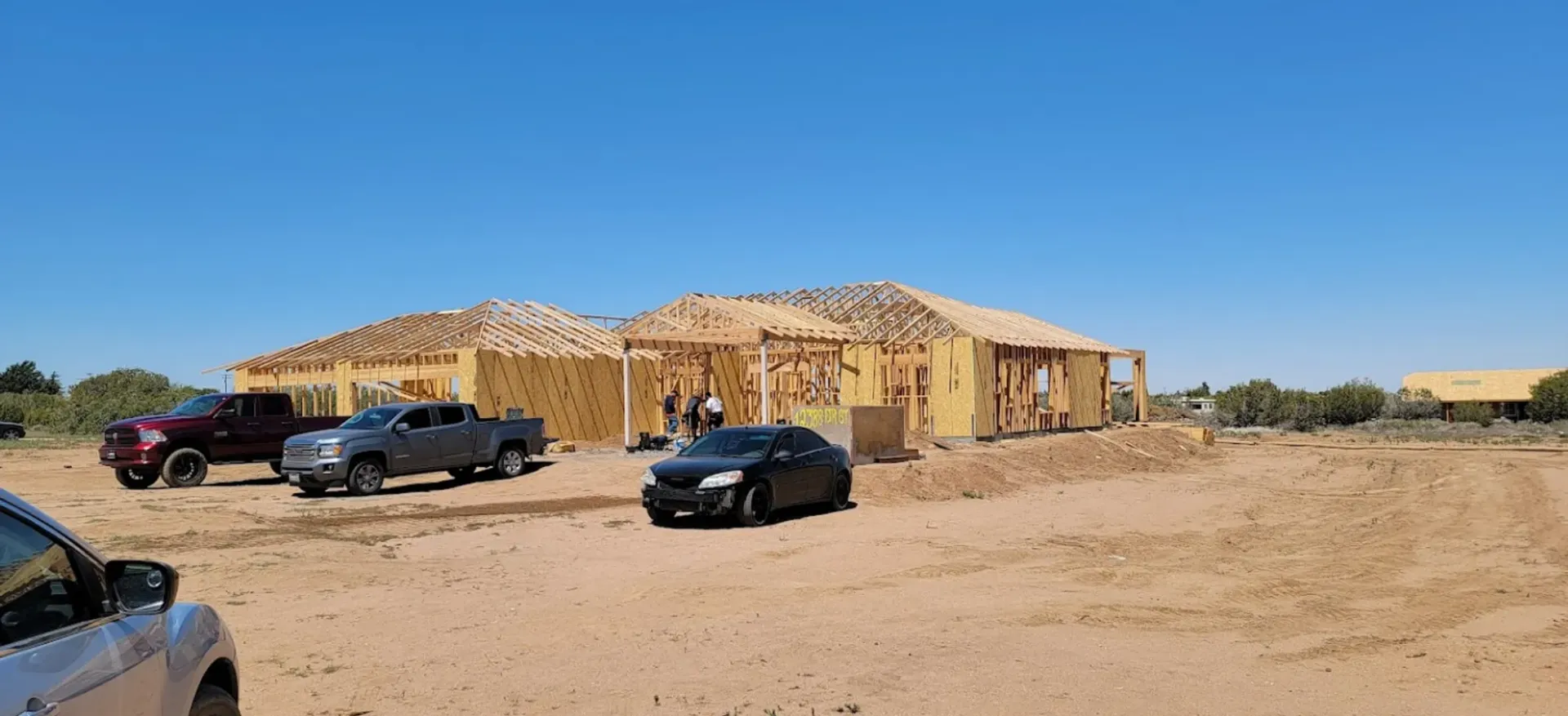 A house is being built in the desert with cars parked in front of it.