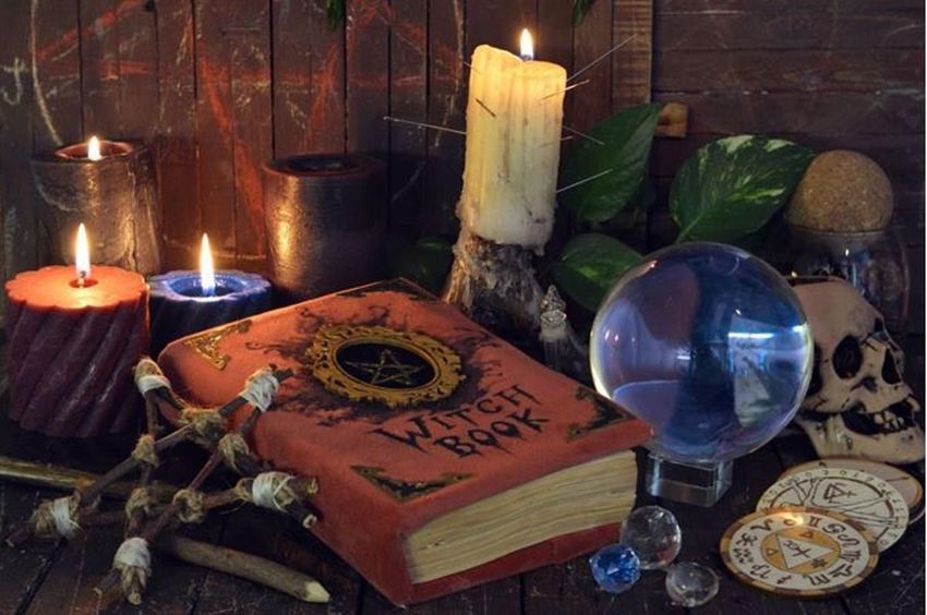 Un libro de brujas está sobre una mesa de madera junto a velas y una bola de cristal.
