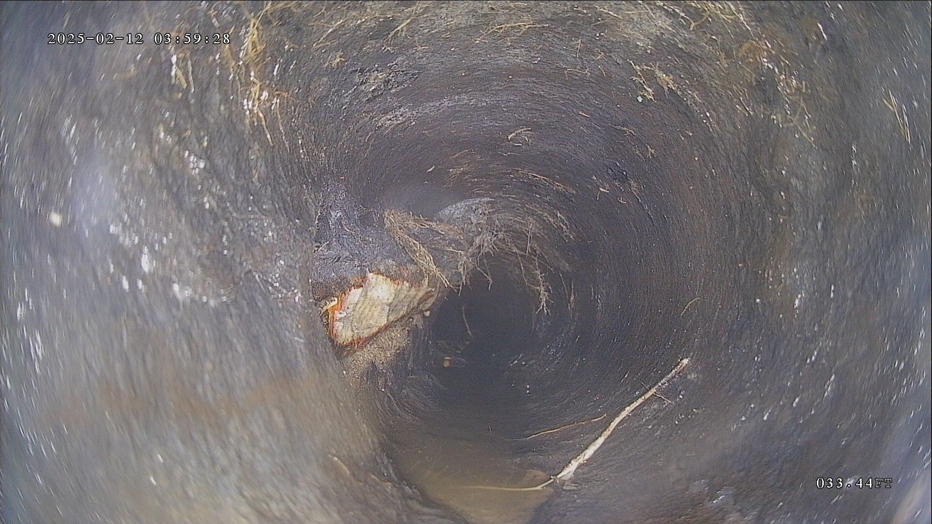 Inside of a dark pipe; debris and corrosion are visible, centered on the view, with swirling water marks around.