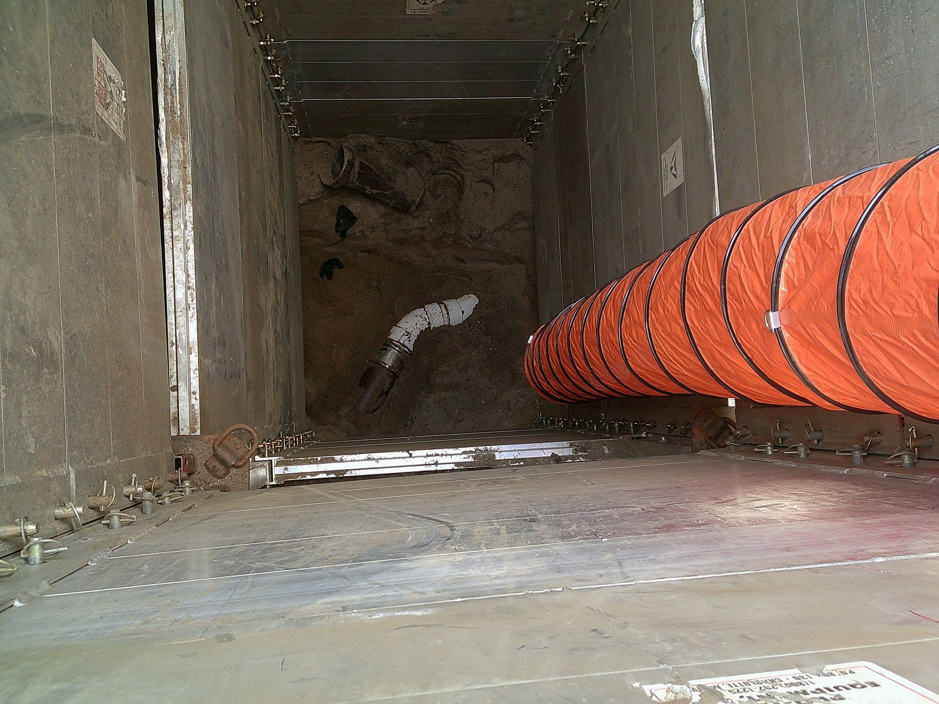 Inside a dark, narrow shaft, an orange ventilation tube hangs to the right, angled towards the back.