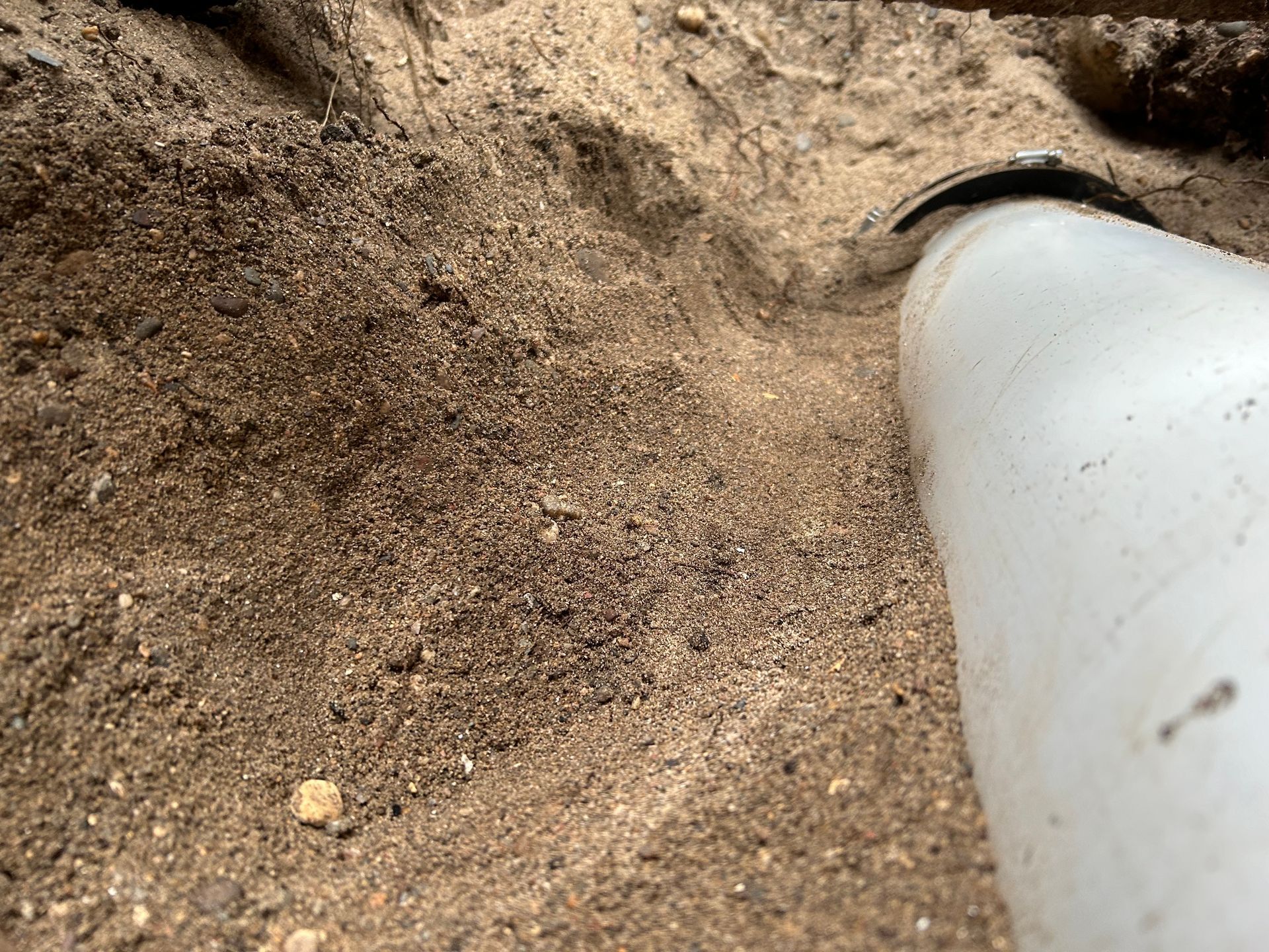 White PVC pipe in a trench filled with sand and small rocks.