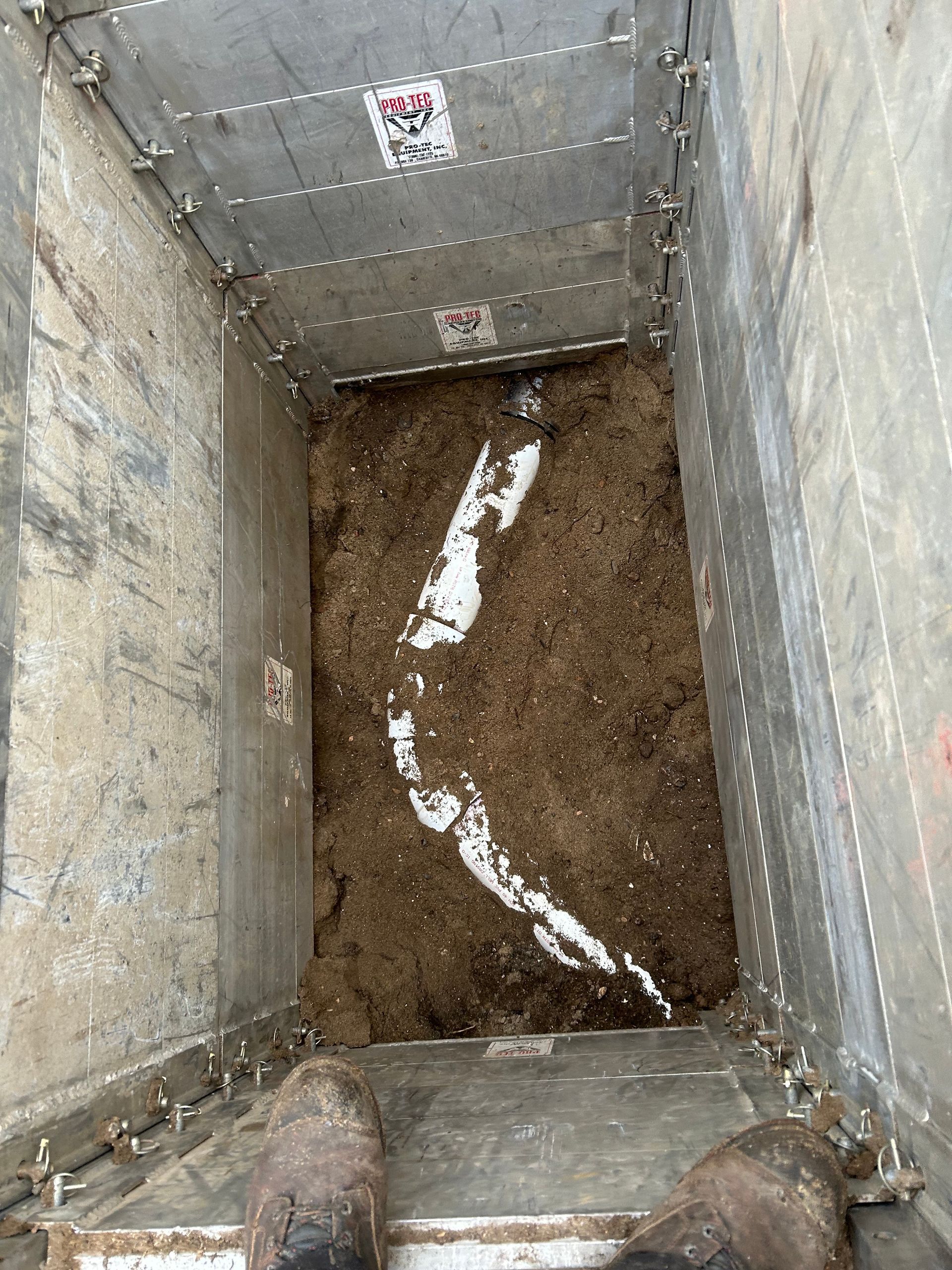 Inside a metal container with brown material and white substance; boots visible at the bottom.