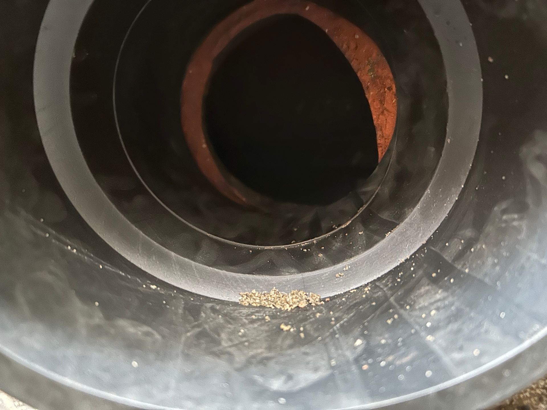 Inside a black pipe, flecks of sand on the bottom. Brown, circular object visible in the center.