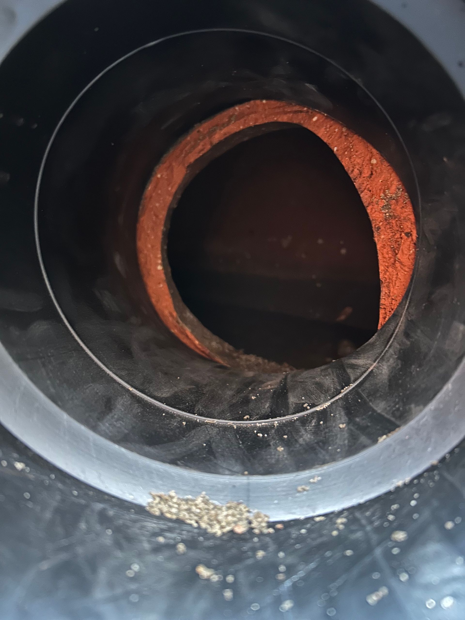 Inside a black pipe: orange inner circle, flecks of debris at the bottom.