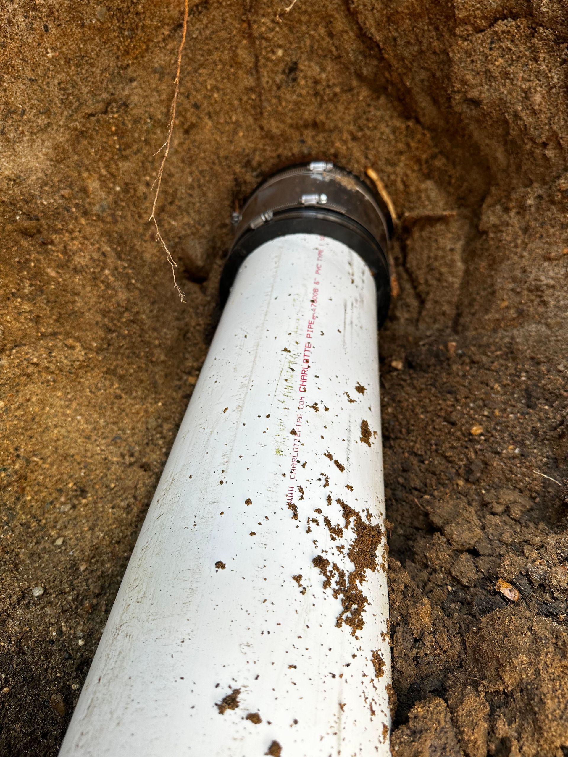 White PVC pipe emerging from the ground, connected to a black fitting. Dirt surrounds the pipe.