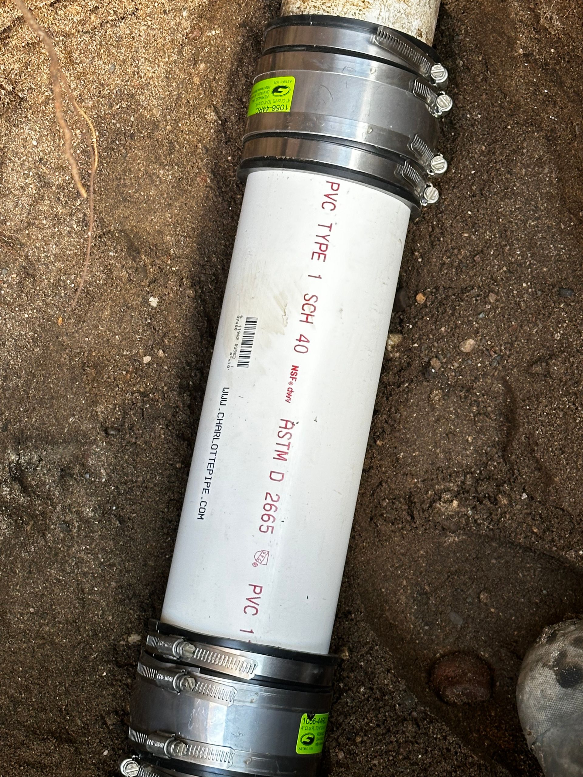 White PVC pipe connecting two other pipes underground.