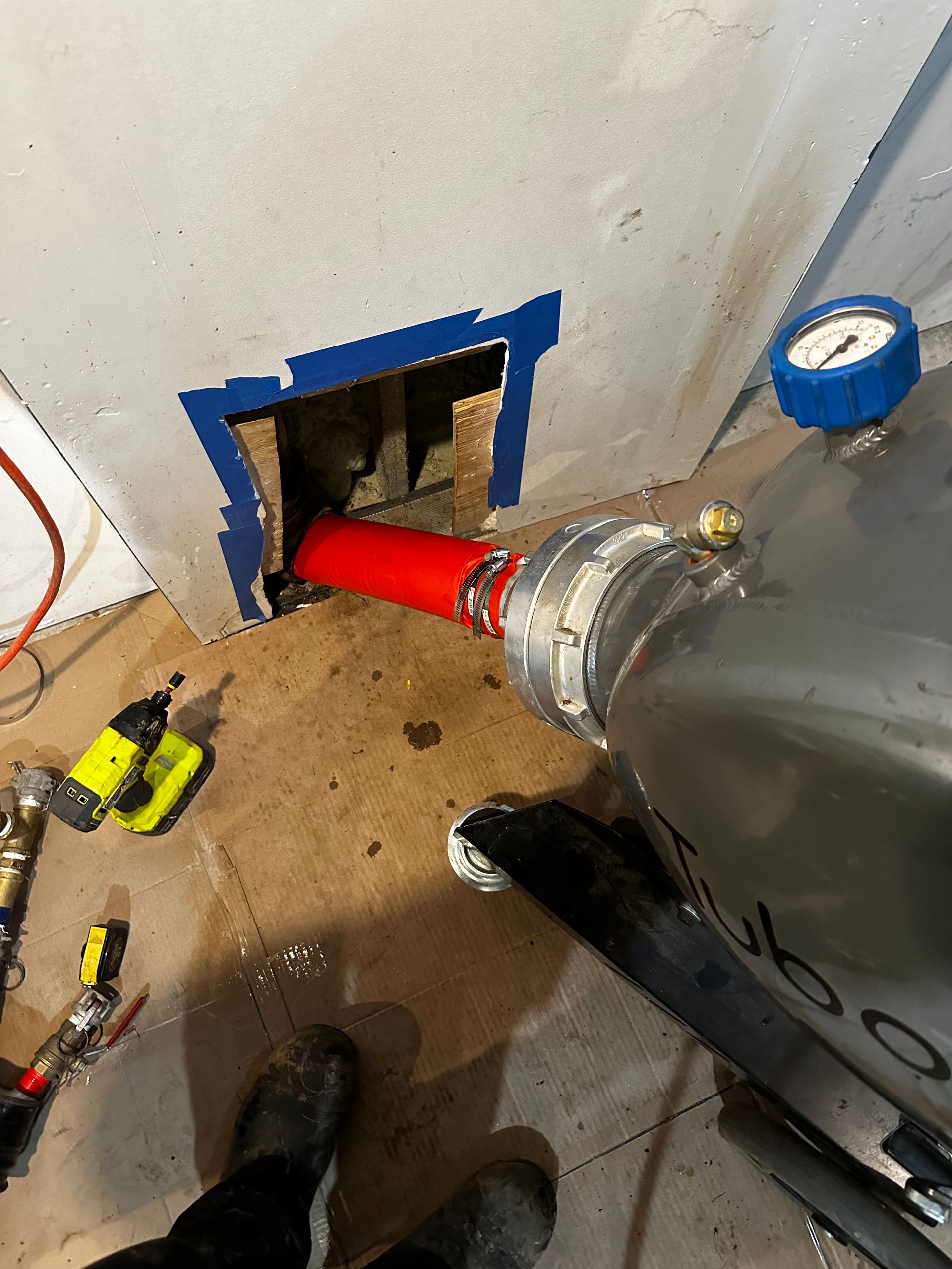 A core drilling machine drills into a wall, with a red pipe extending out. Tools and debris surround it.