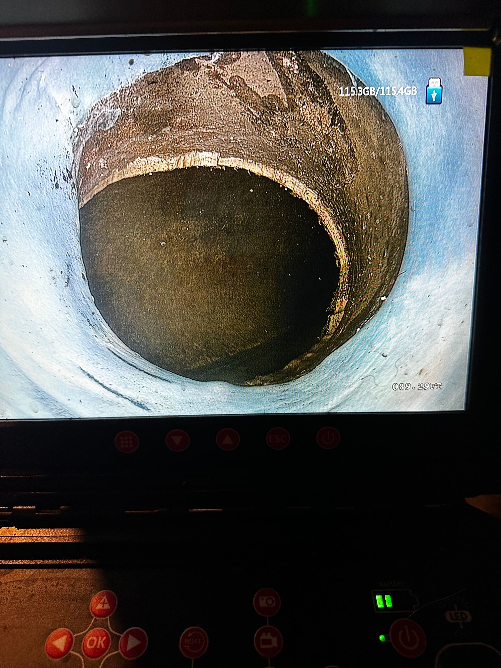 View from a camera inside a pipe. A dark pipe opening is surrounded by a dirty, circular surface.
