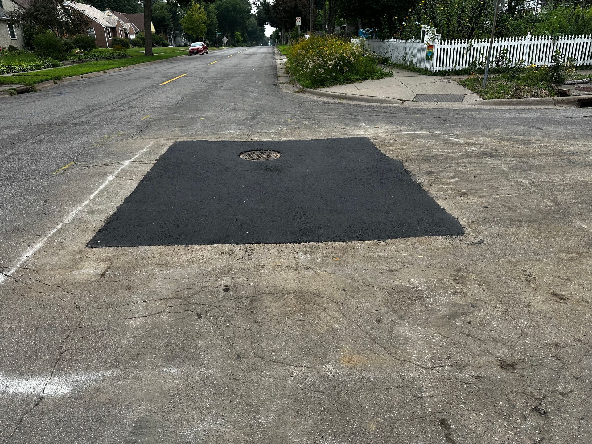 Asphalt patch on a worn street with a manhole cover in the center.