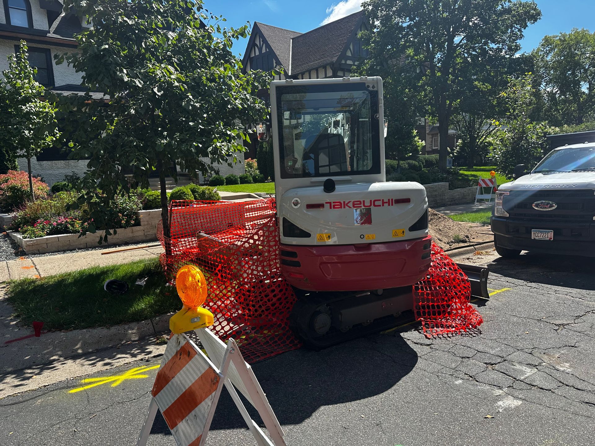 Mini excavator on street behind orange construction barriers.