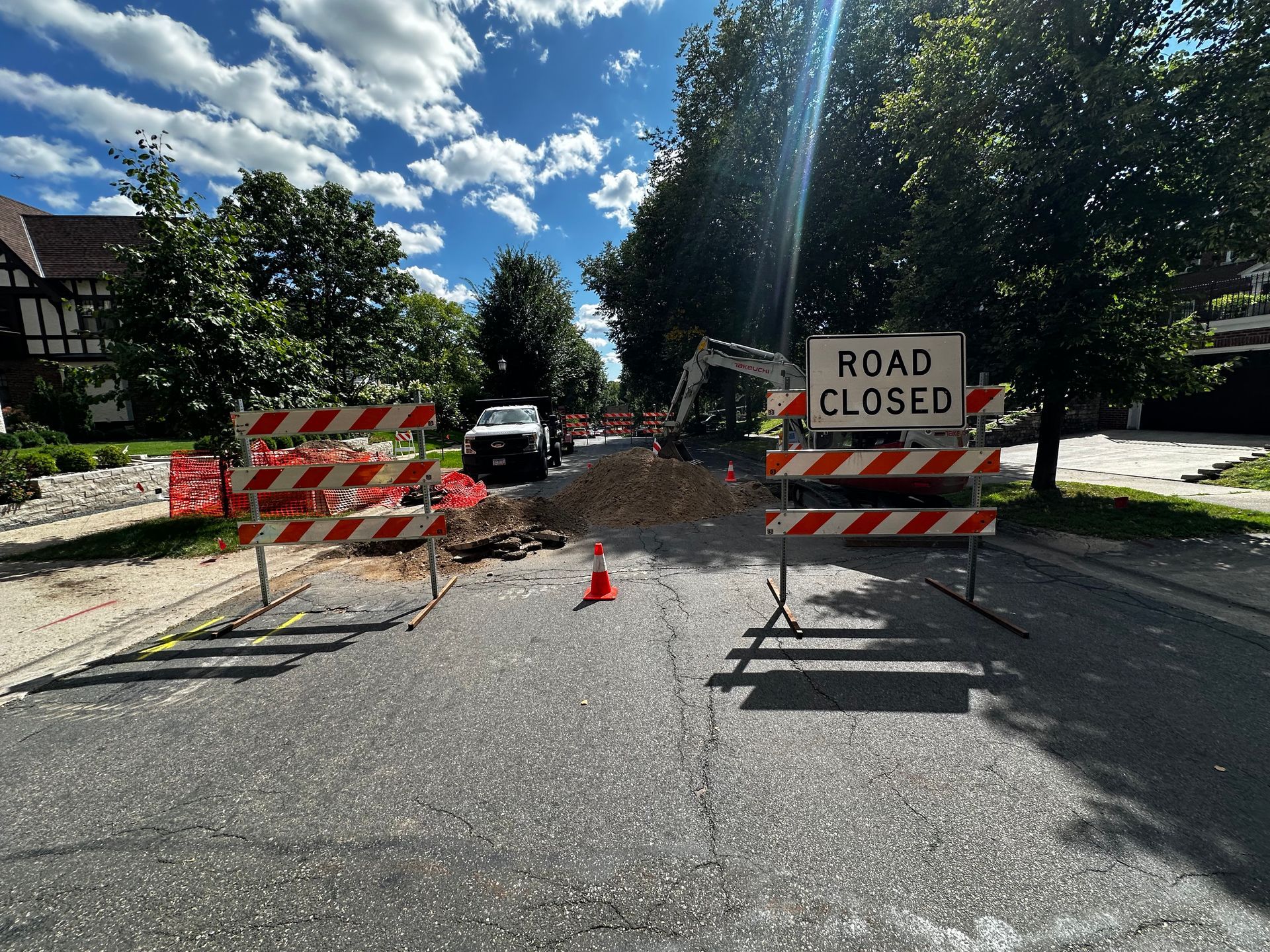 Road closed due to construction. Barricades, cones, and a sign block a street. A pile of gravel sits in the middle.