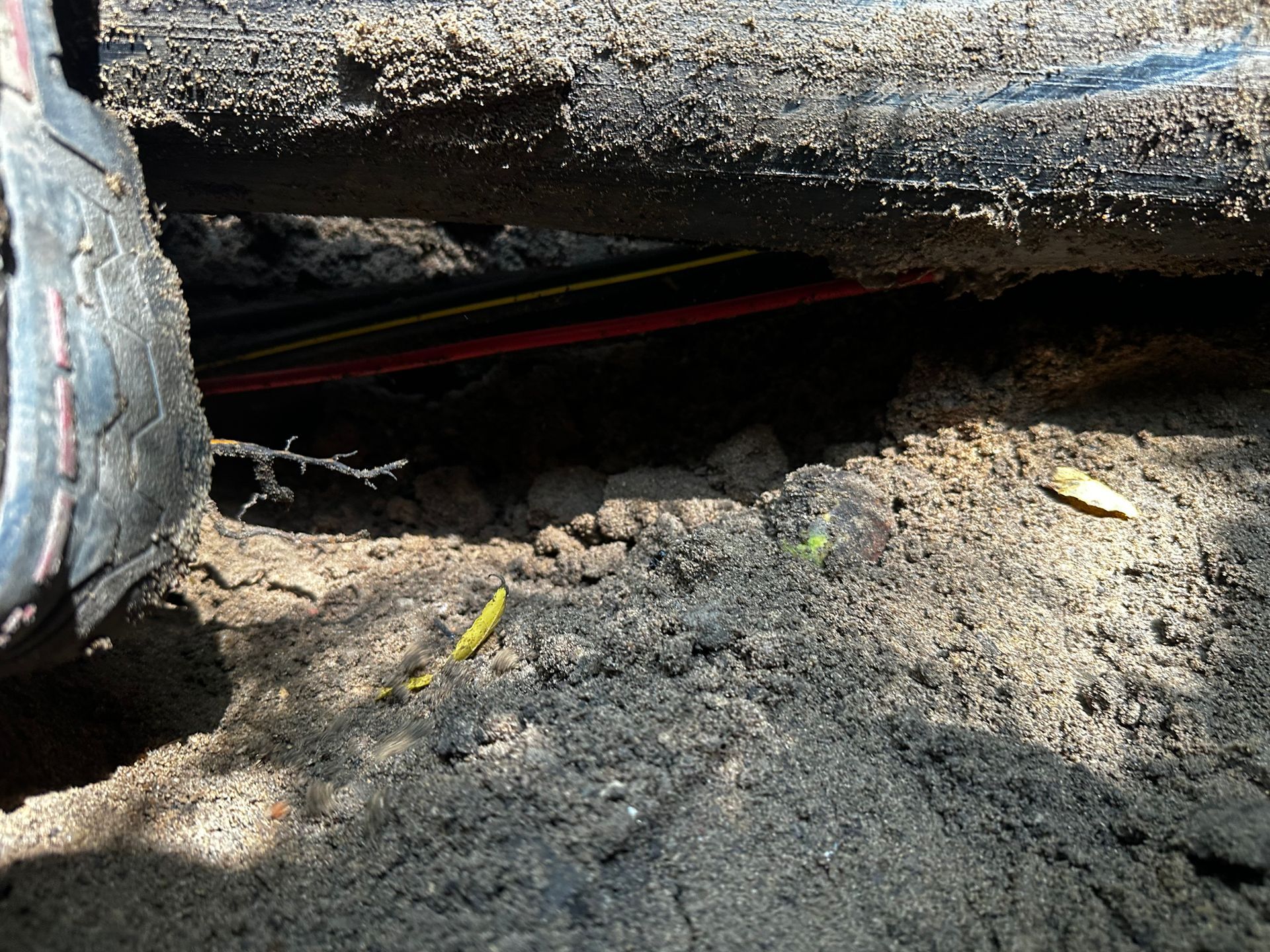 A tire on the left casts a shadow over dark soil and underground cables with red and yellow lines.