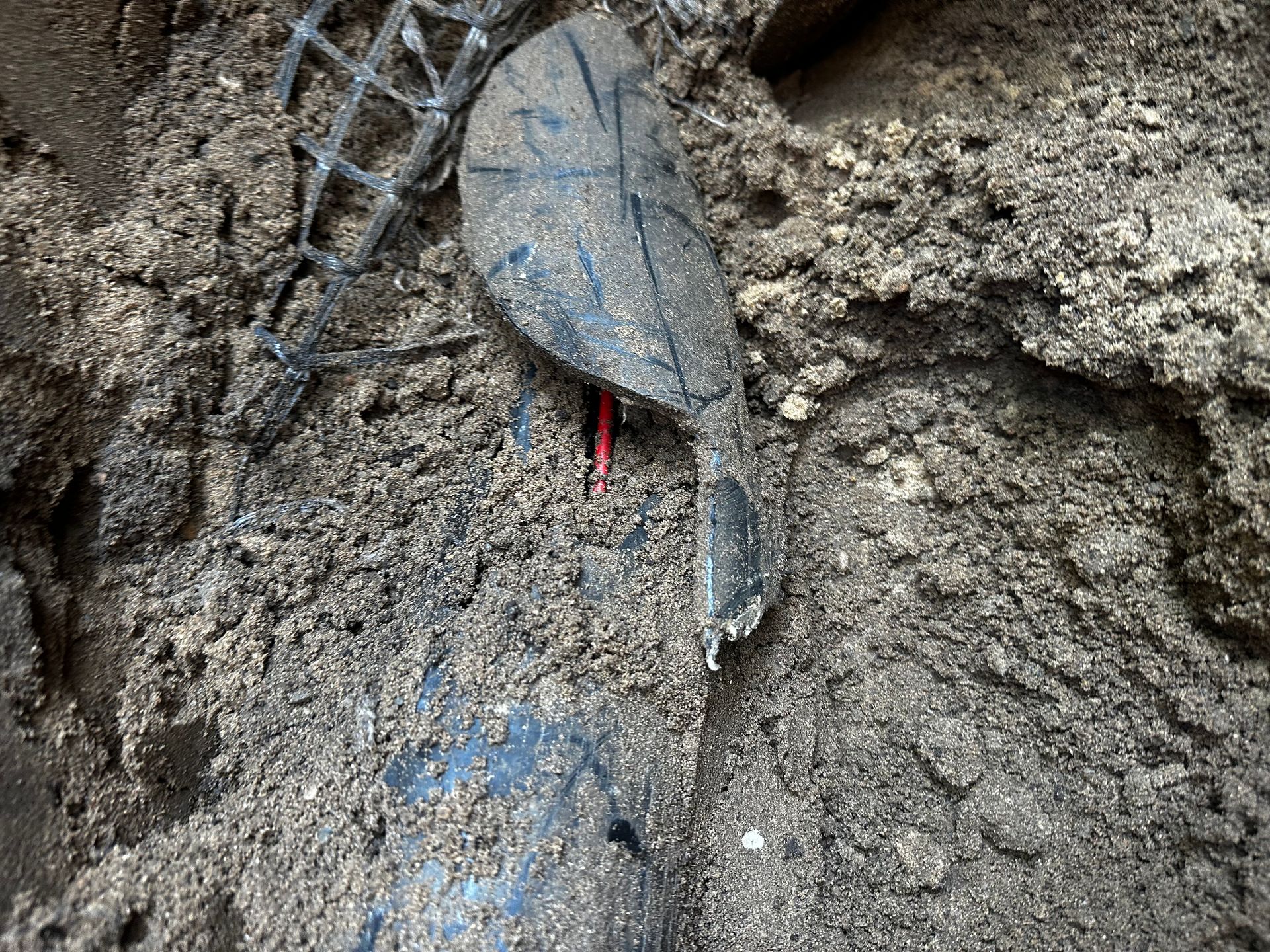Black plastic pipe and debris in soil; a red wire is visible.