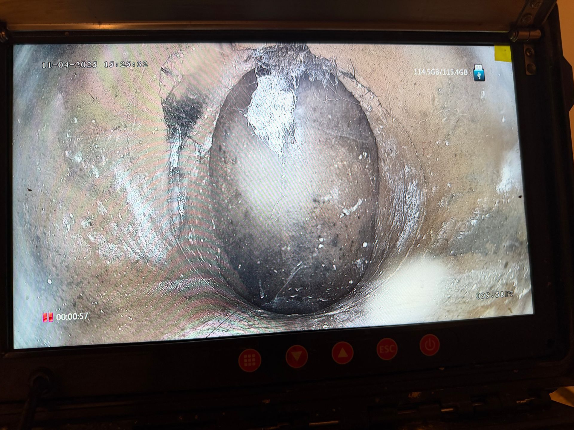 Screen displaying a close-up of a dark, oval-shaped object within a pipe, possibly a blockage.