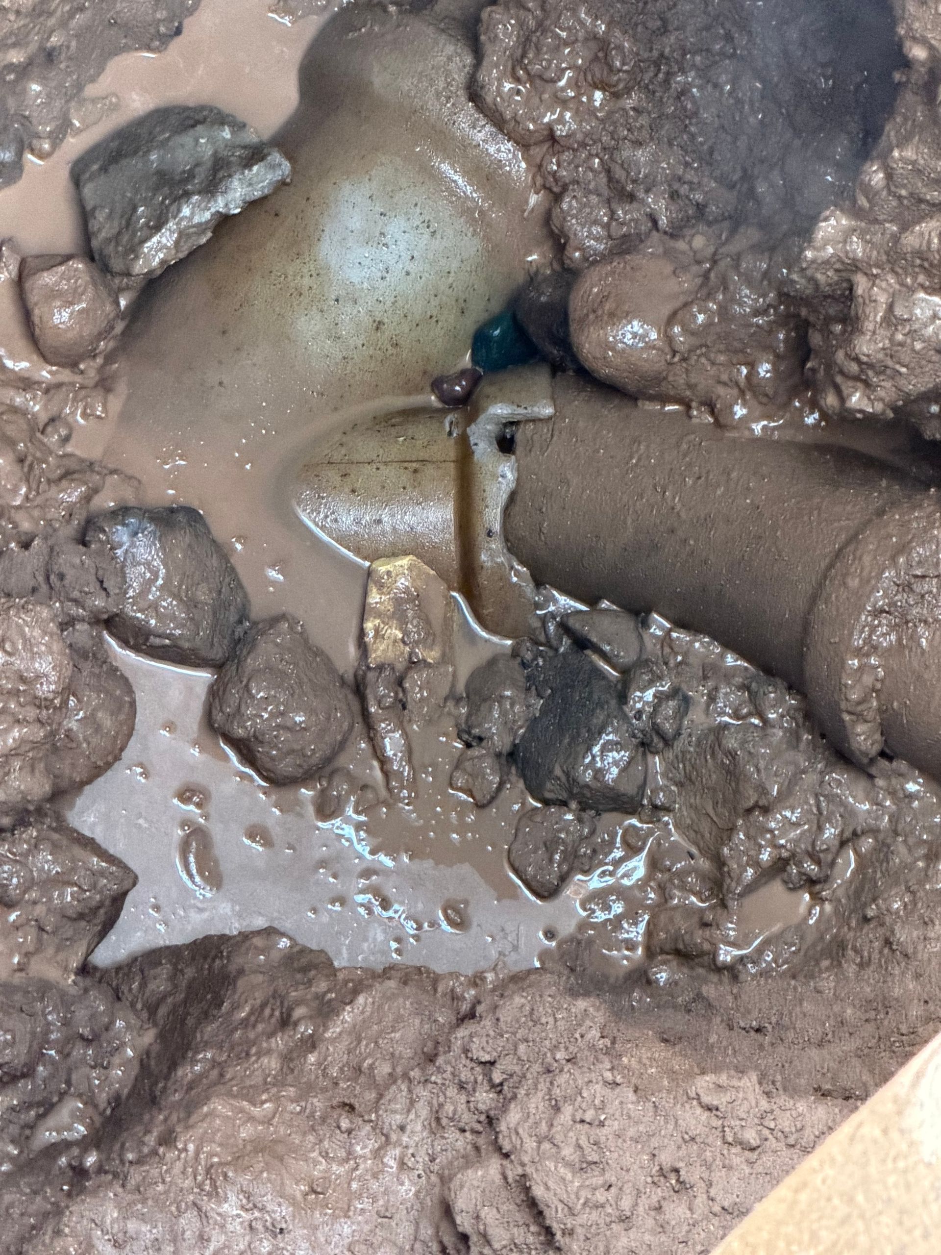 Broken pipe submerged in muddy water and surrounded by rocks.