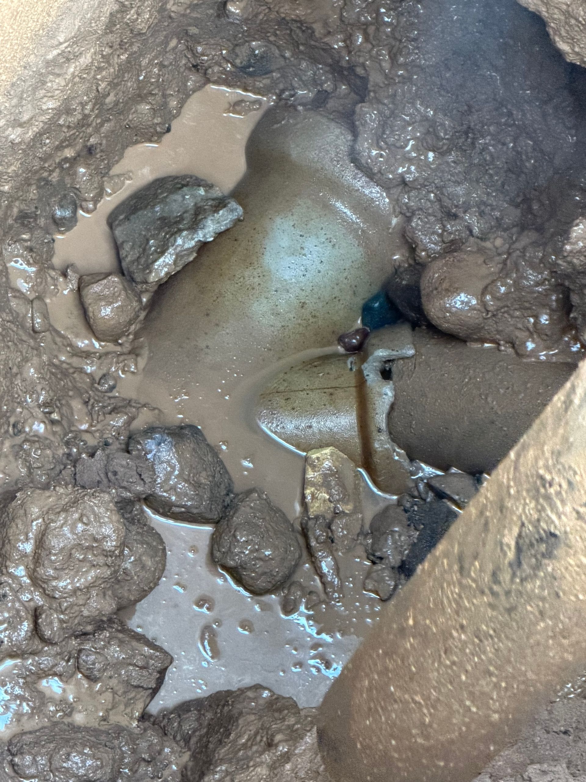 A broken pipe in muddy ground, surrounded by rocks and standing water.